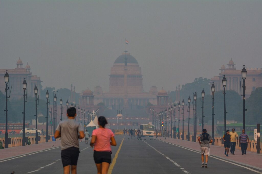 People jogging in smog near Rashtrapati Bhavan, New Delhi, highlighting urban pollution.