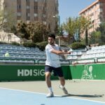 Male tennis player hitting a ball on an urban outdoor court during the day.