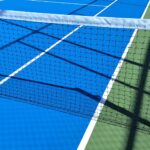 Close-up view of a tennis court with blue and green surfaces, featuring the net and shadows.