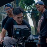 Group of filmmakers reviewing footage on set outdoors, focused on camera equipment.