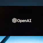 Minimalist display of OpenAI logo on a screen, set against a gradient blue background.