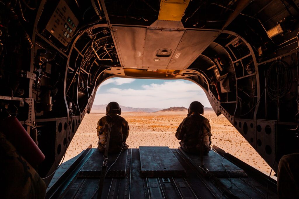 Soldiers seated in helicopter looking over a vast desert landscape.