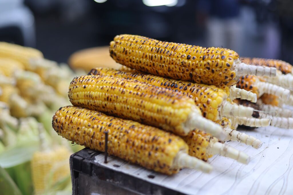Close-up of freshly grilled corn cobs stacked in an outdoor street market setting.