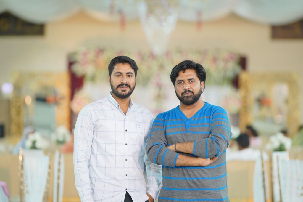 Two men standing indoors at an elegant event in Kasur, Punjab.
