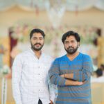 Two men standing indoors at an elegant event in Kasur, Punjab.