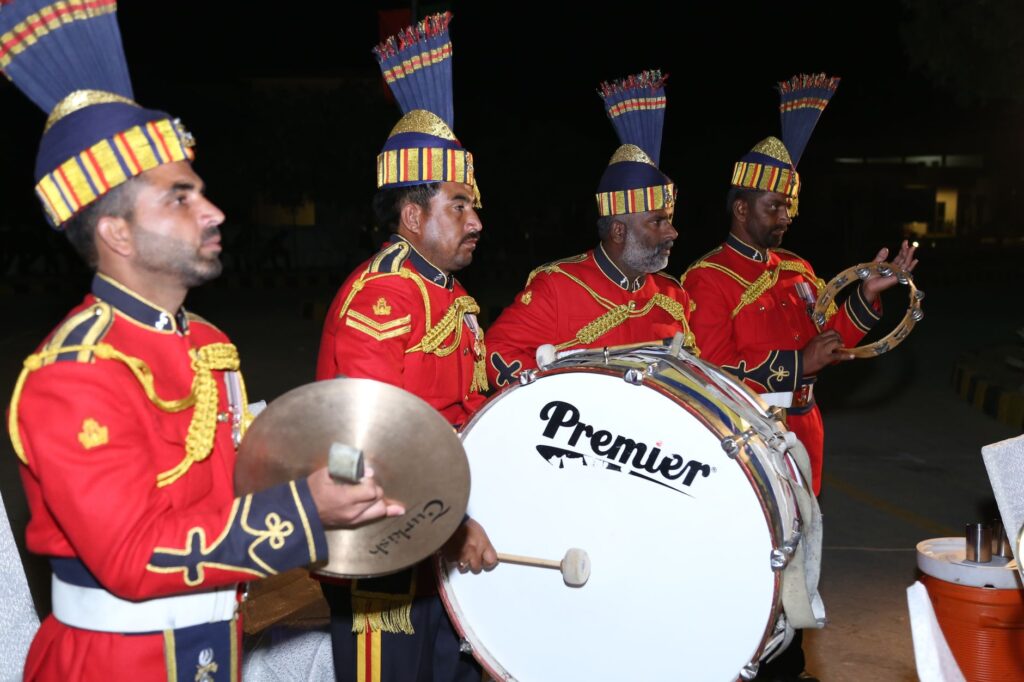 Vibrant military band performing at night with cymbals, drums, and tambourine outdoors.