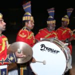 Vibrant military band performing at night with cymbals, drums, and tambourine outdoors.