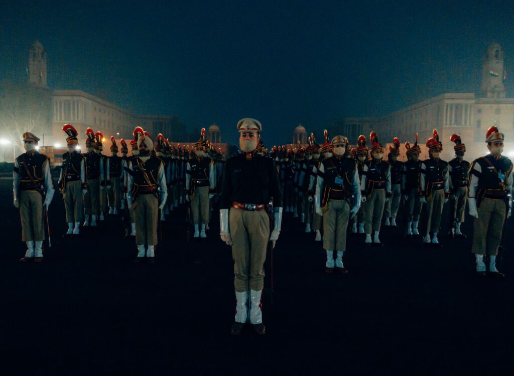 A group of soldiers in uniform stand in formation during a nighttime parade.