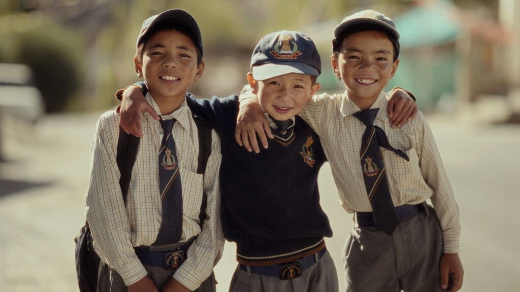 Three schoolboys wearing uniforms smiling on a sunny day, representing friendship and youth.
