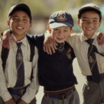 Three schoolboys wearing uniforms smiling on a sunny day, representing friendship and youth.