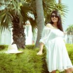 Pregnant woman in white dress enjoying a sunny day outdoors by a hedge.