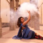 Woman in blue dress posing dramatically with smoke in a historic stone structure.