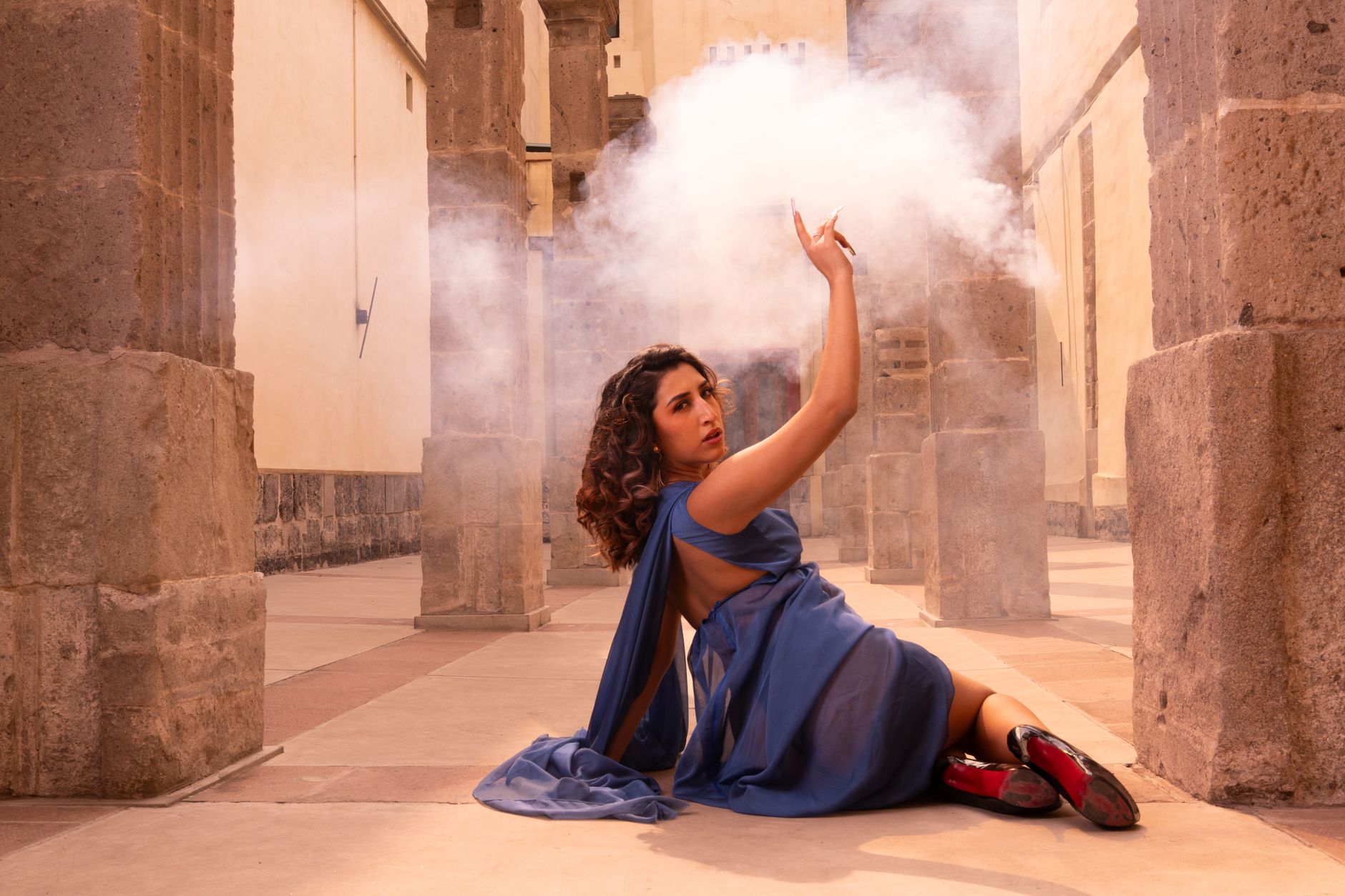 Woman in blue dress posing dramatically with smoke in a historic stone structure.