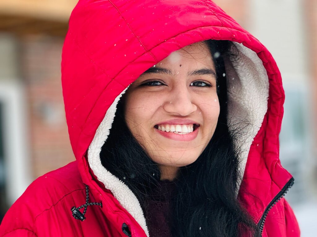 Young woman smiling outdoors in a red winter jacket with snowflakes.