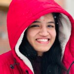 Young woman smiling outdoors in a red winter jacket with snowflakes.