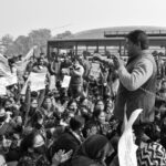 A black and white image capturing a protest crowd with a passionate speaker addressing the gathering.