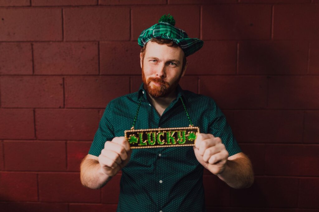 Bearded man celebrating St. Patrick's Day with a lucky necklace and green attire.