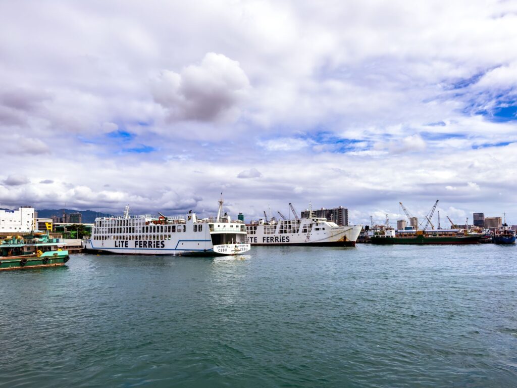 Ferry boats docked at a bustling harbor in Cebu City, under a partly cloudy sky.