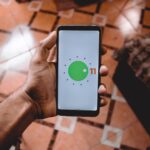 Close-up of a hand holding a smartphone displaying Android 11 interface indoors on patterned floor.
