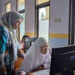A female teacher guides a student working on a computer in a school lab, fostering learning.