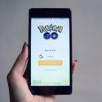 Smartphone displaying Pokémon Go app sign-in screen, held in hand.