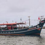 A beautiful Indian fishing boat with colorful flags sails on a cloudy day, showcasing maritime culture.