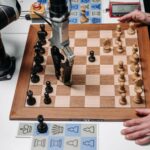 A robotic arm playing chess against a human hand on an electronic chessboard indoors.