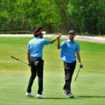 Two men on a golf course in Hyderabad high-fiving after a successful play.