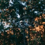 A drone hovering mid-air against a blurred autumn forest background.
