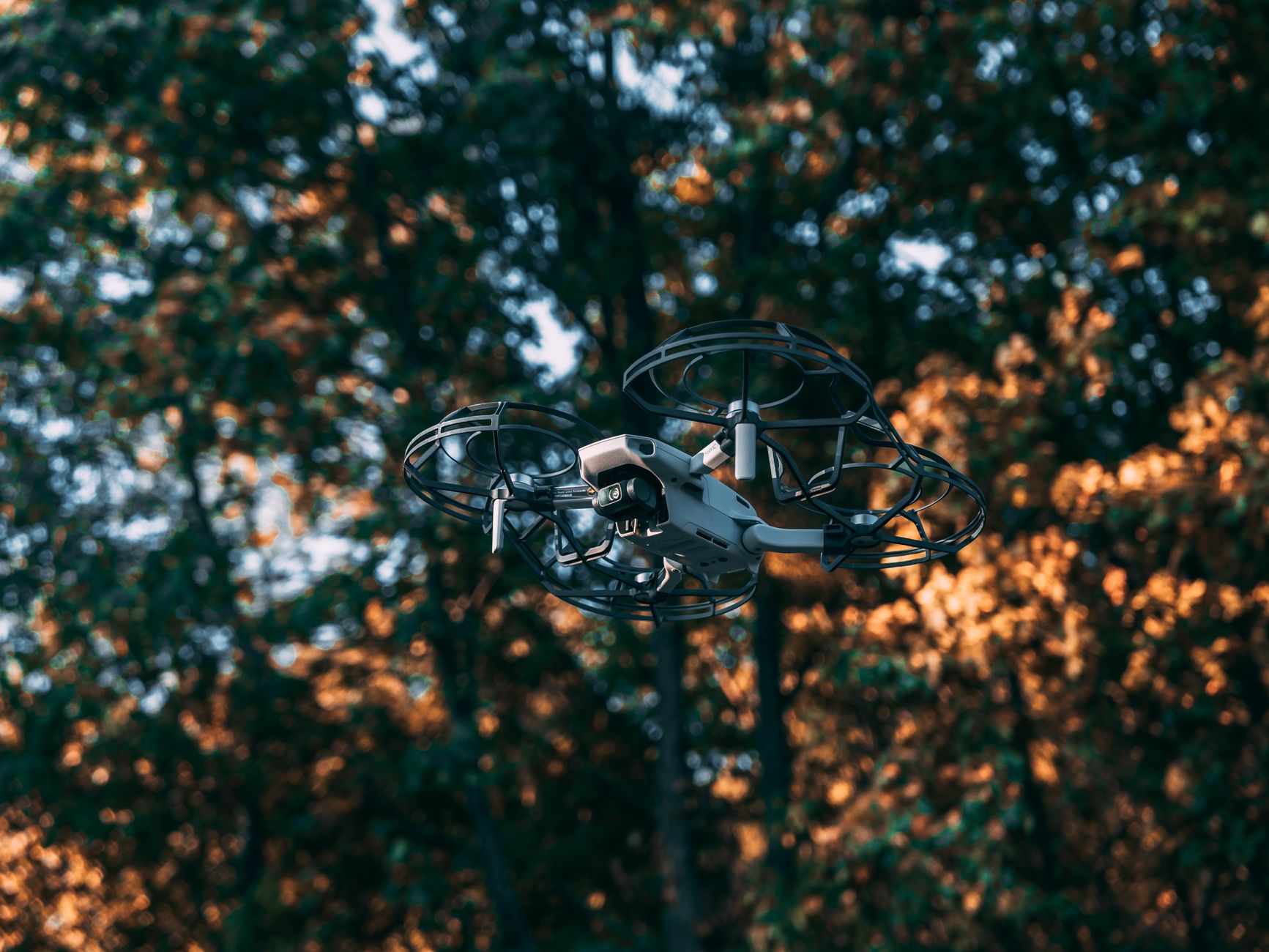 A drone hovering mid-air against a blurred autumn forest background.