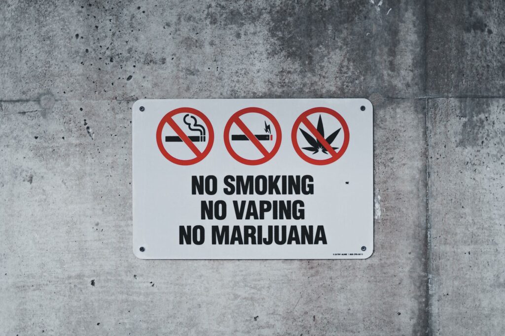 A clear warning sign prohibiting smoking, vaping, and marijuana on a concrete wall.