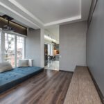 Blue soft mattress with colorful cushions near window against wall with modern TV in spacious apartment with projector and kitchen