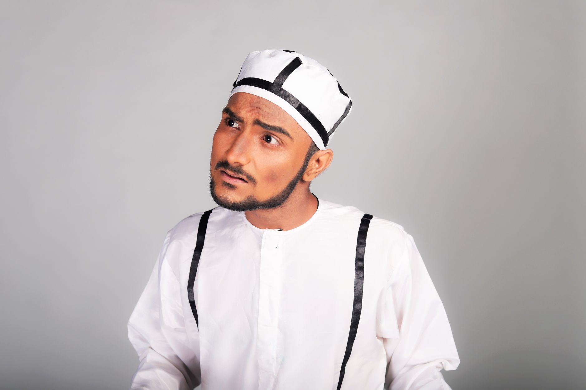 Portrait of a South Asian man in traditional attire with a curious expression. Studio shot.