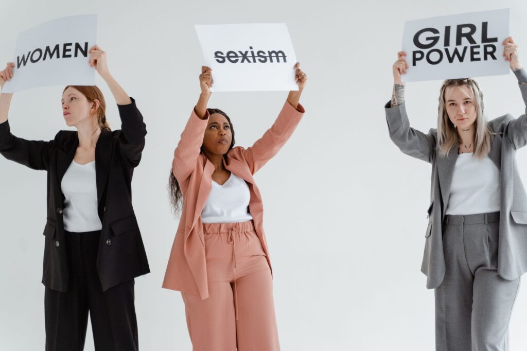 Three women in business attire hold signs promoting feminism and gender equality.