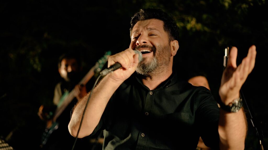 Bearded man in black shirt passionately singing with microphone during performance.