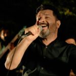 Bearded man in black shirt passionately singing with microphone during performance.