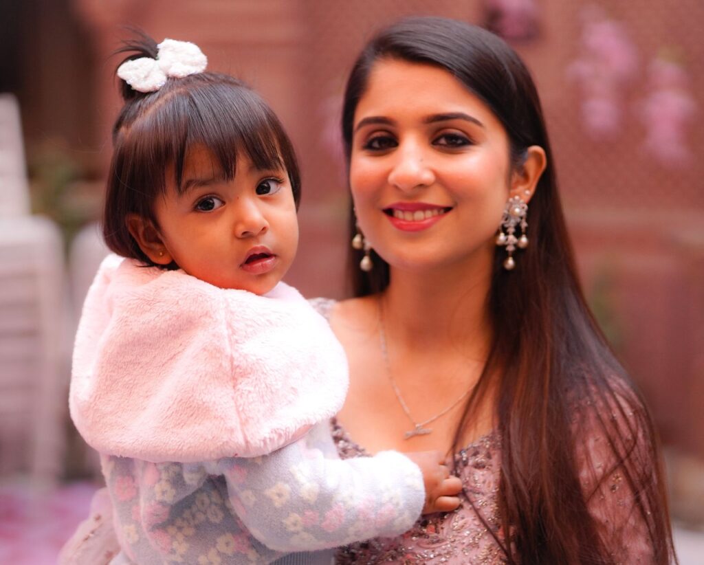 A joyful mother holds her adorable baby, both smiling against a blurred outdoor backdrop.