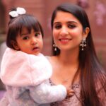 A joyful mother holds her adorable baby, both smiling against a blurred outdoor backdrop.