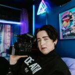 Portrait of a person holding a vintage camcorder in a neon-lit room, capturing a retro vibe.