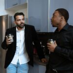 Two men having a casual discussion while enjoying coffee in an office kitchen setting.