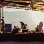 Musicians preparing outdoor stage during sunset with equipment and instruments.