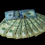 A fanned-out stack of hundred dollar U.S. banknotes on a black background.