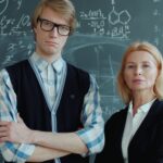 Two teachers standing confidently in front of a blackboard filled with math equations.