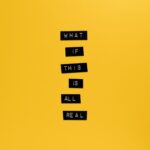 Inspirational text 'What if this is all real' on yellow surface.
