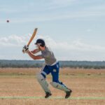 Cricketer in action hitting the ball outdoors on a sunny day.