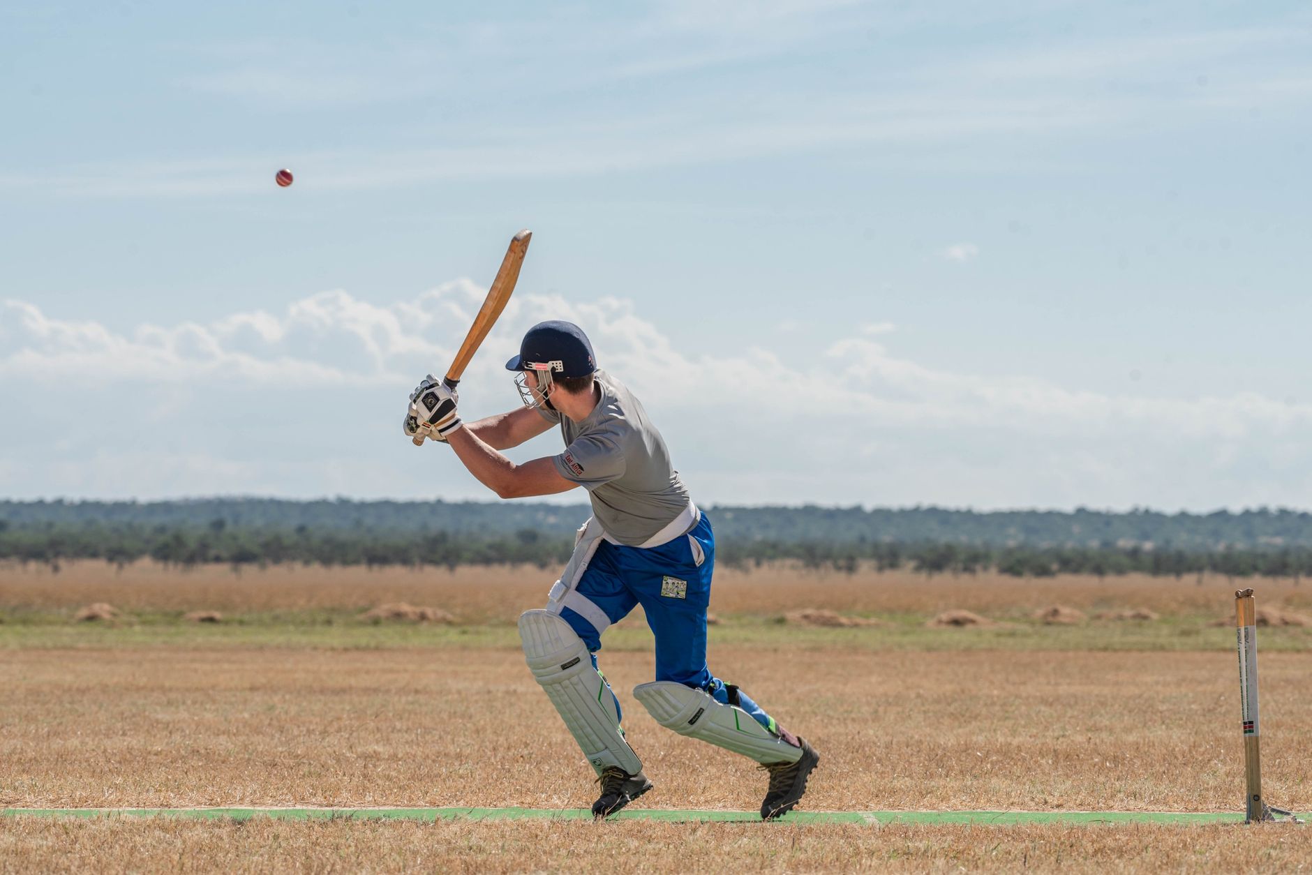 Cricketer in action hitting the ball outdoors on a sunny day.