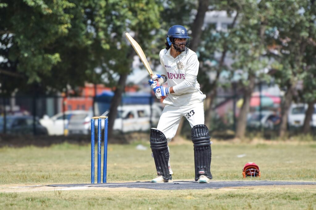 Batsman poised to strike in a cricket match, set outdoors on a sunny day.