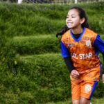 A young girl in vibrant sportswear joyfully running on a green field during soccer practice.