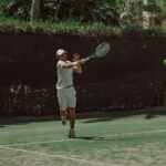 Male tennis player hitting a forehand shot on an outdoor court during a sunny day.