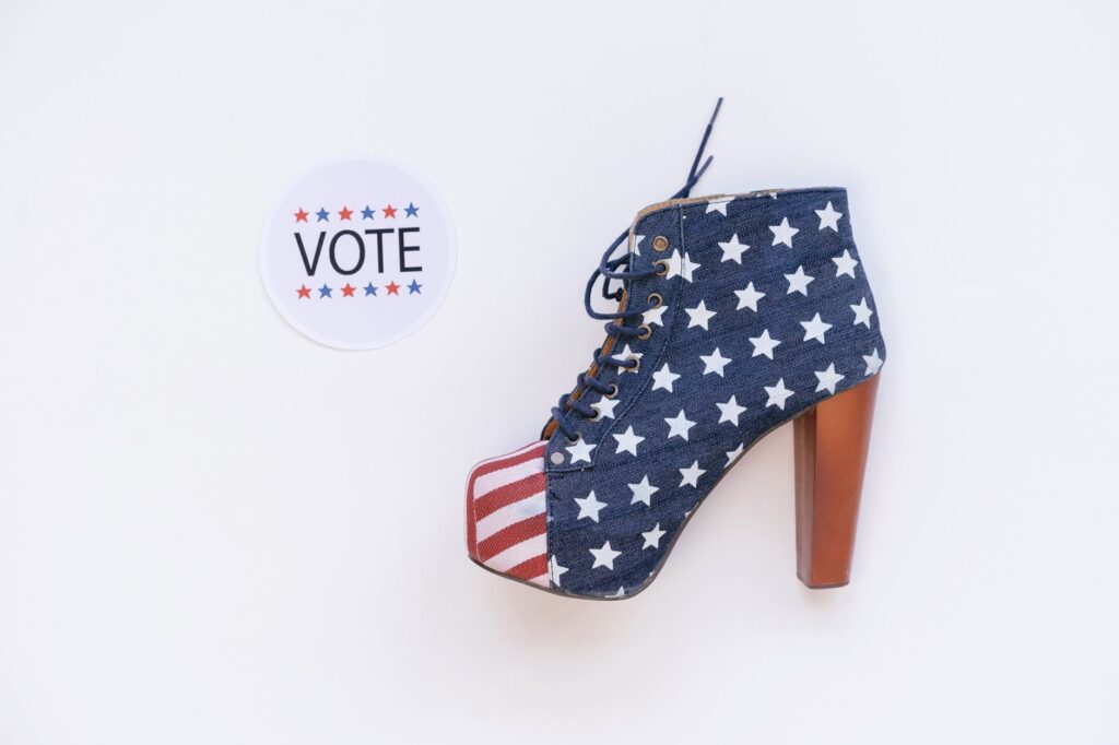 High heel with American flag design beside a voting sticker on white background.